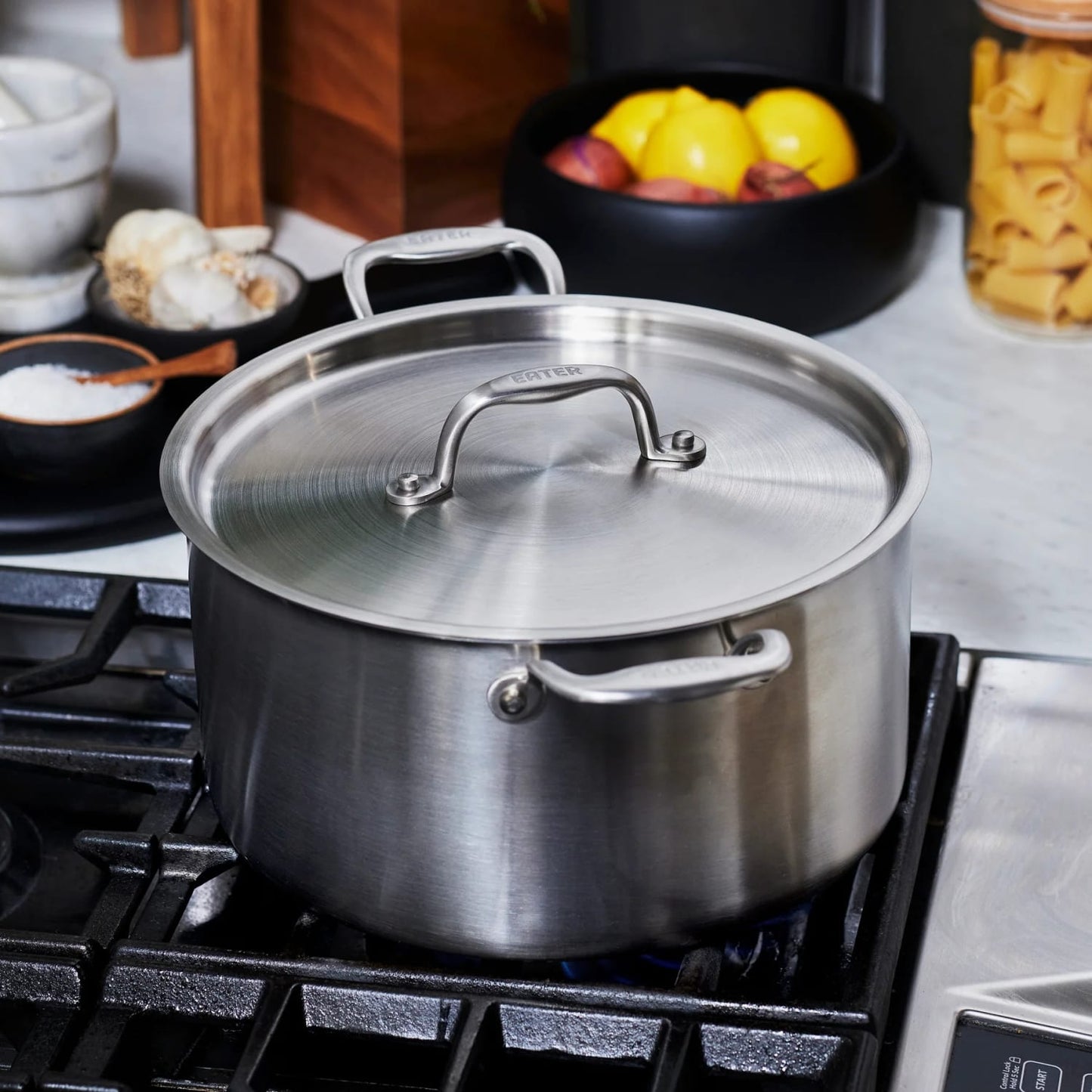 Fully clad stainless steel stock pot with lid on gas stove, featured in kitchenware and kitchen gadgets collections