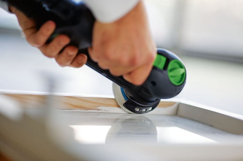 Person using a compact sanding tool with edge protector on a wood window frame in home improvement tools collection
