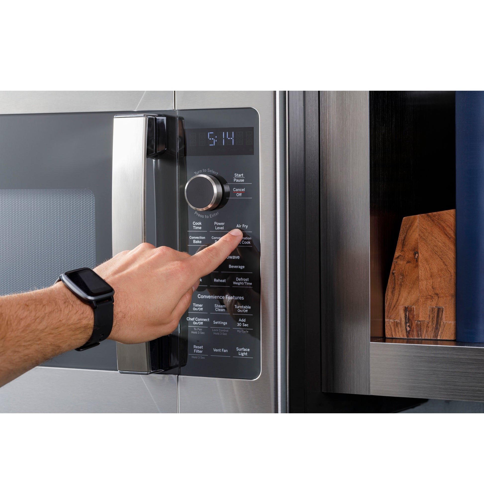 Person pressing control panel buttons on stainless steel over-the-range microwave in modern kitchen setting
