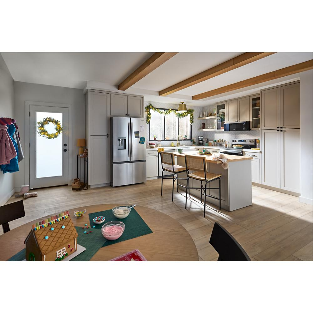Spacious kitchen with beige cabinetry, stainless steel refrigerator, wooden beams, and festive holiday decorations near natural light windows