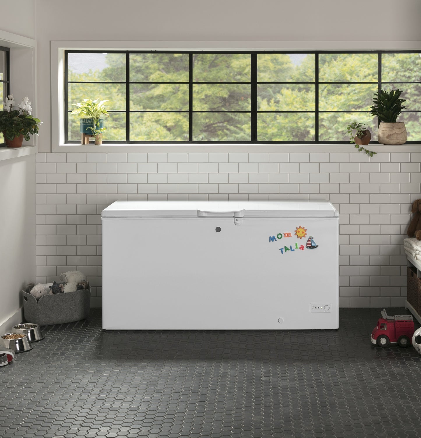White chest freezer with child-friendly colorful magnets in modern kitchen with tiled walls and large window