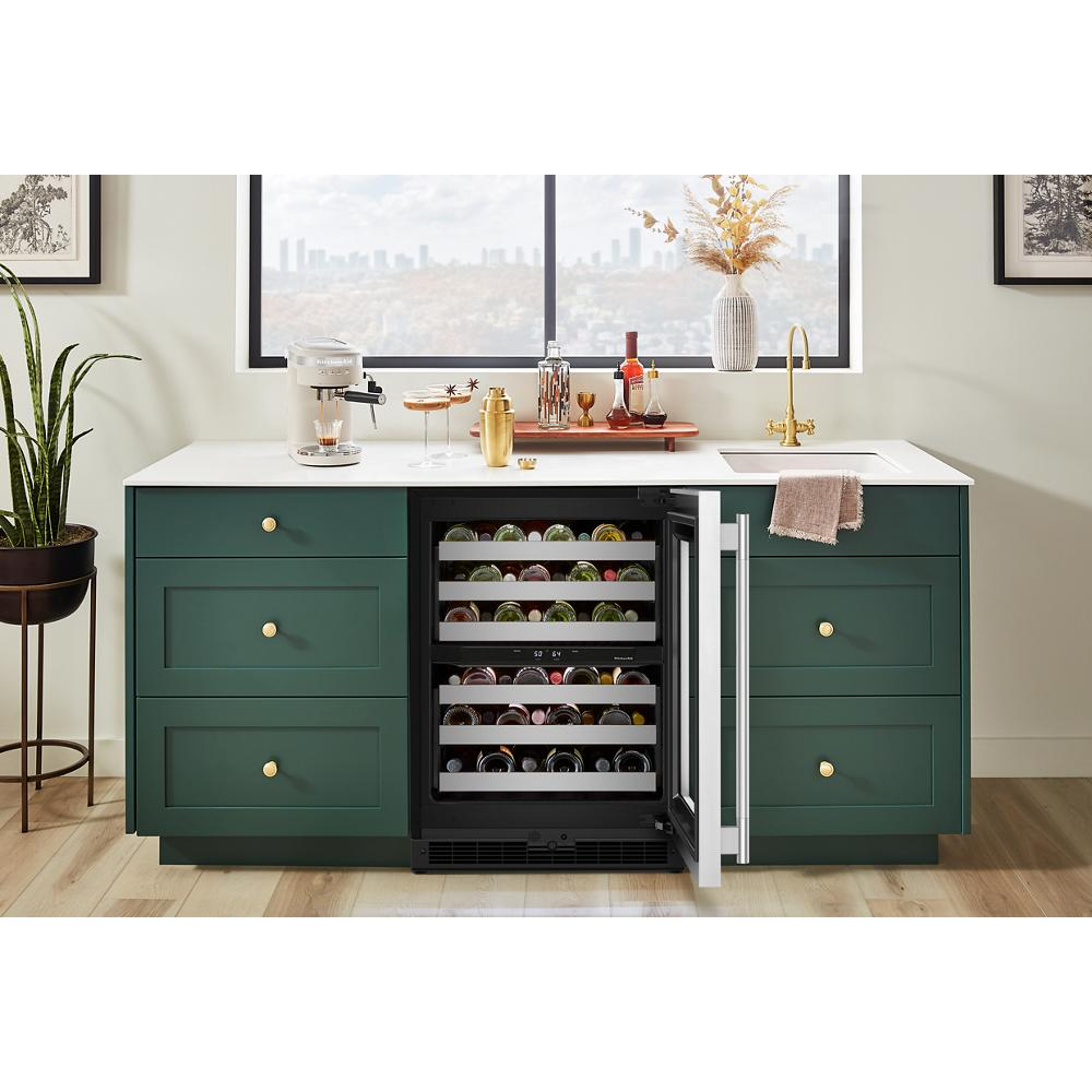 Open undercounter wine cellar with full-extension metal-front racks inside green kitchen cabinetry under white countertop in bright room