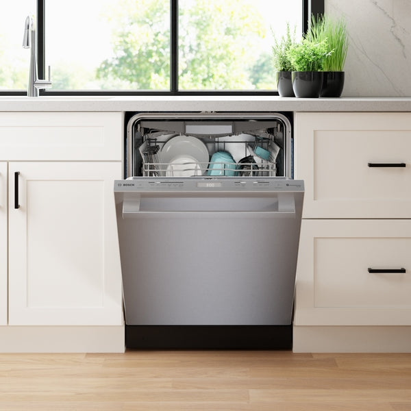 Open stainless steel dishwasher integrated into white cabinetry in modern kitchen with natural light and plants on counter