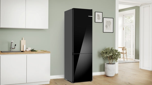 Sleek black free-standing fridge-freezer with bottom freezer and glass door in a modern kitchen setting with green walls.