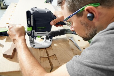 Person using a Festool OF 1010 REBQ-Set+FS router on wood with dust extraction in a home improvement workshop setting
