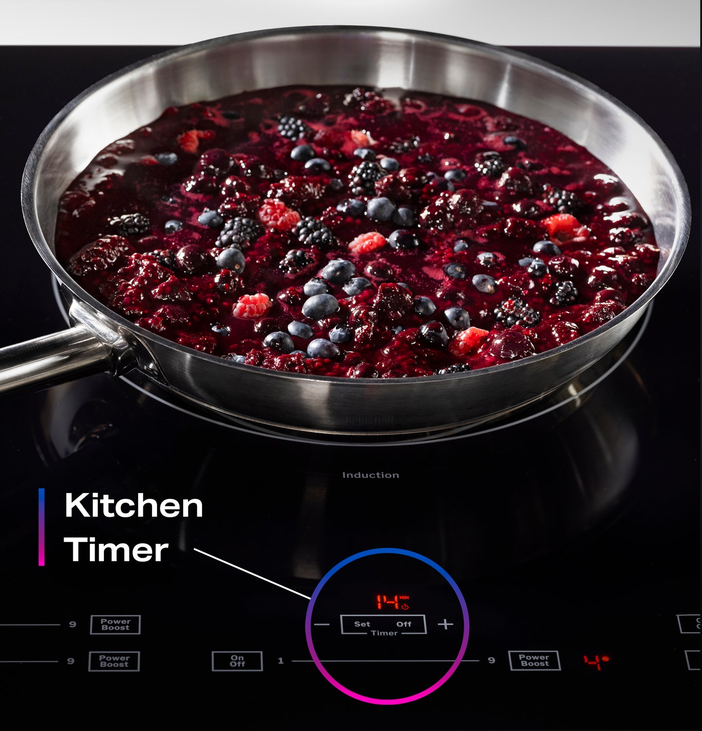 Stainless steel pan simmering mixed berries on black induction cooktop with digital timer control for kitchen use