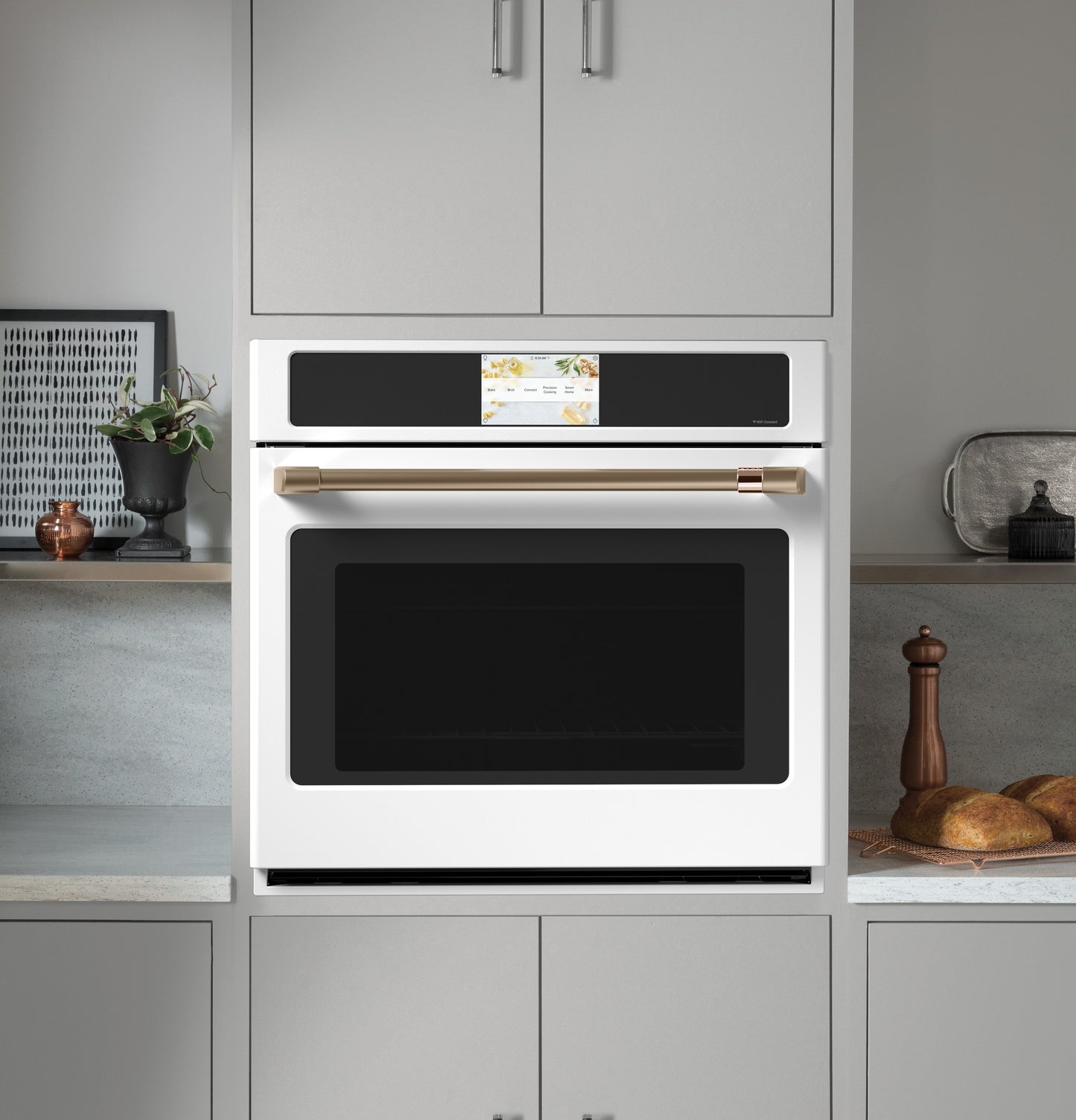 White built-in convection wall oven with touchscreen and brass handle in modern kitchen cabinetry setting