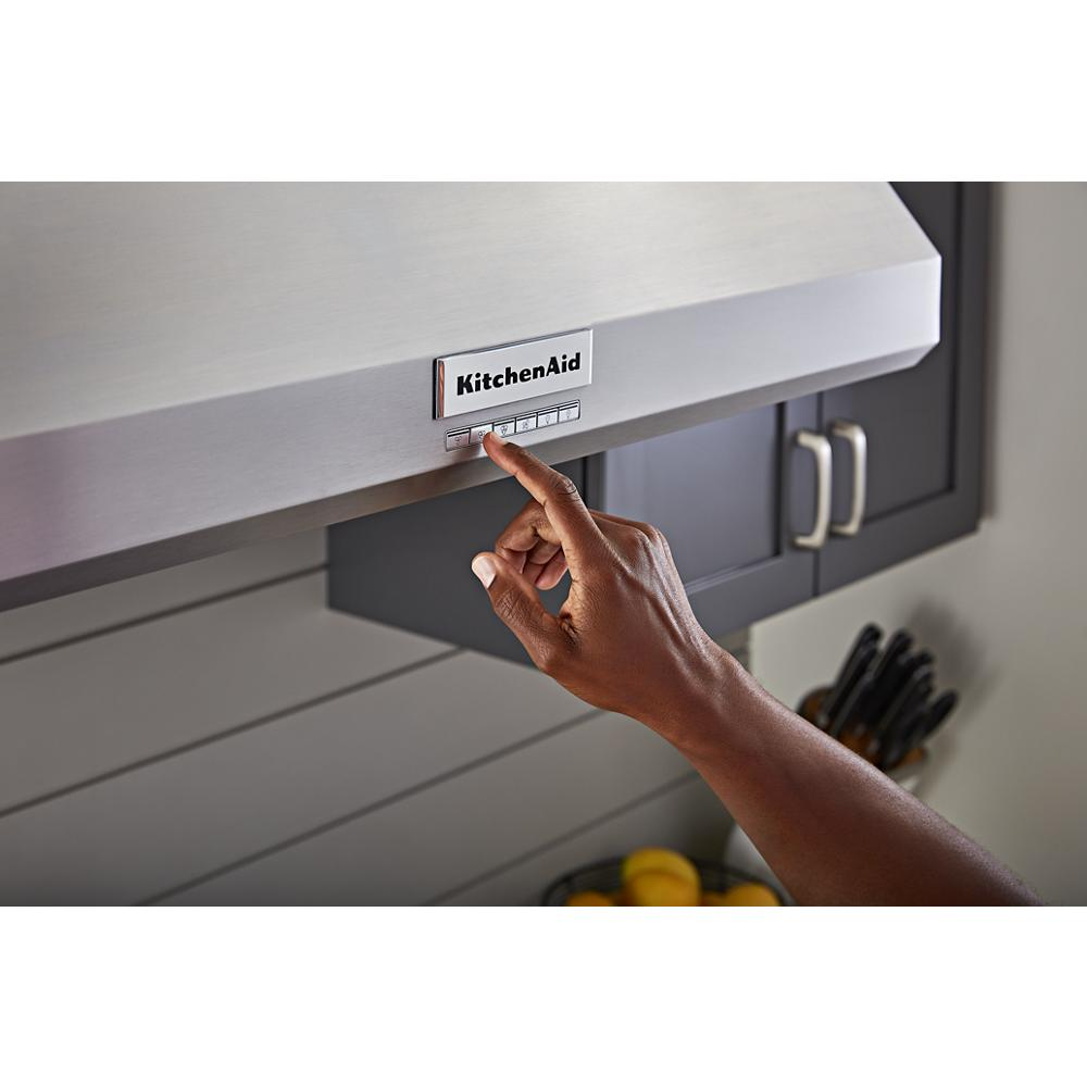 Hand pressing control buttons on stainless steel commercial-style wall-mount range hood in kitchen setting