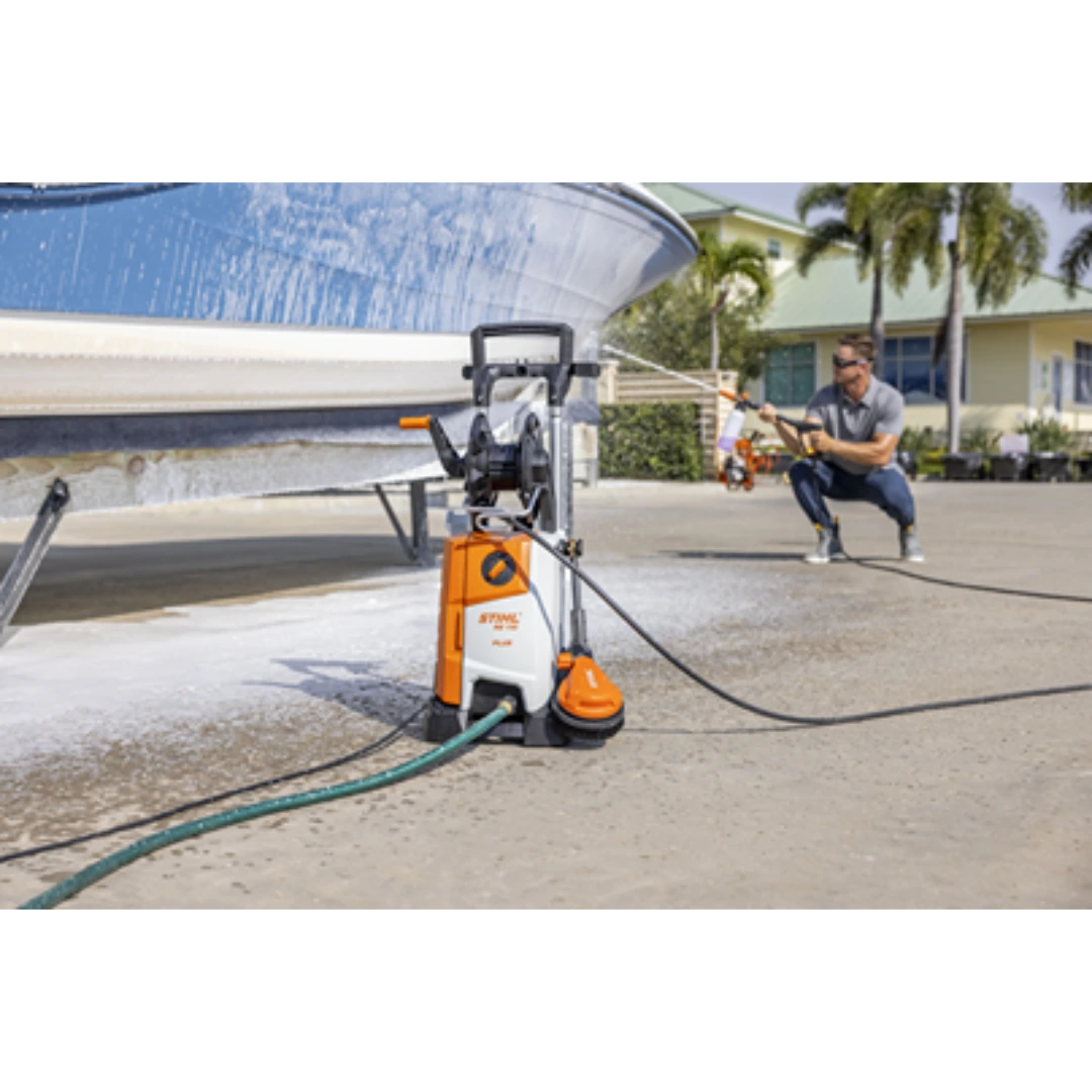 Orange and white STIHL pressure washer with hose reel cleaning a boat on a driveway in a residential area