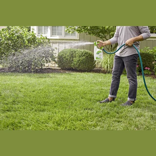 Person spraying Scotts Turf Builder Starter Food on a green lawn in a residential lawn care setting
