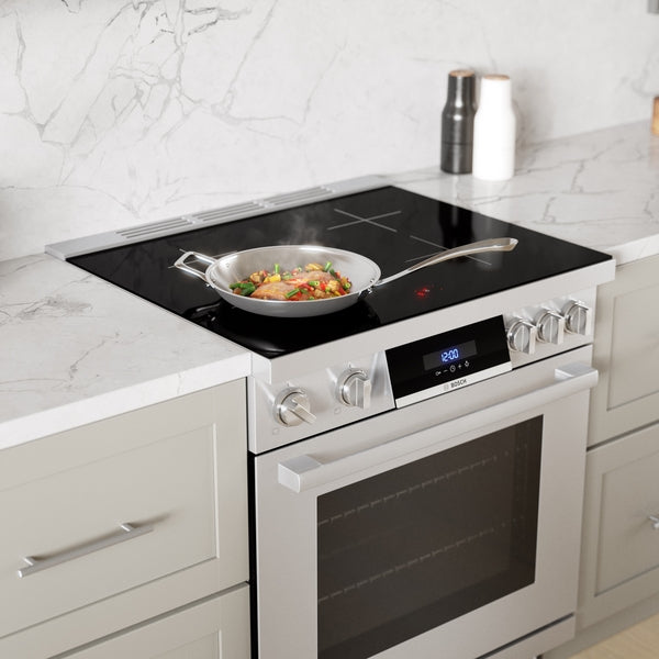 Induction freestanding range with frameless glass surface, ergonomic display, and metal knobs in a modern kitchen setting