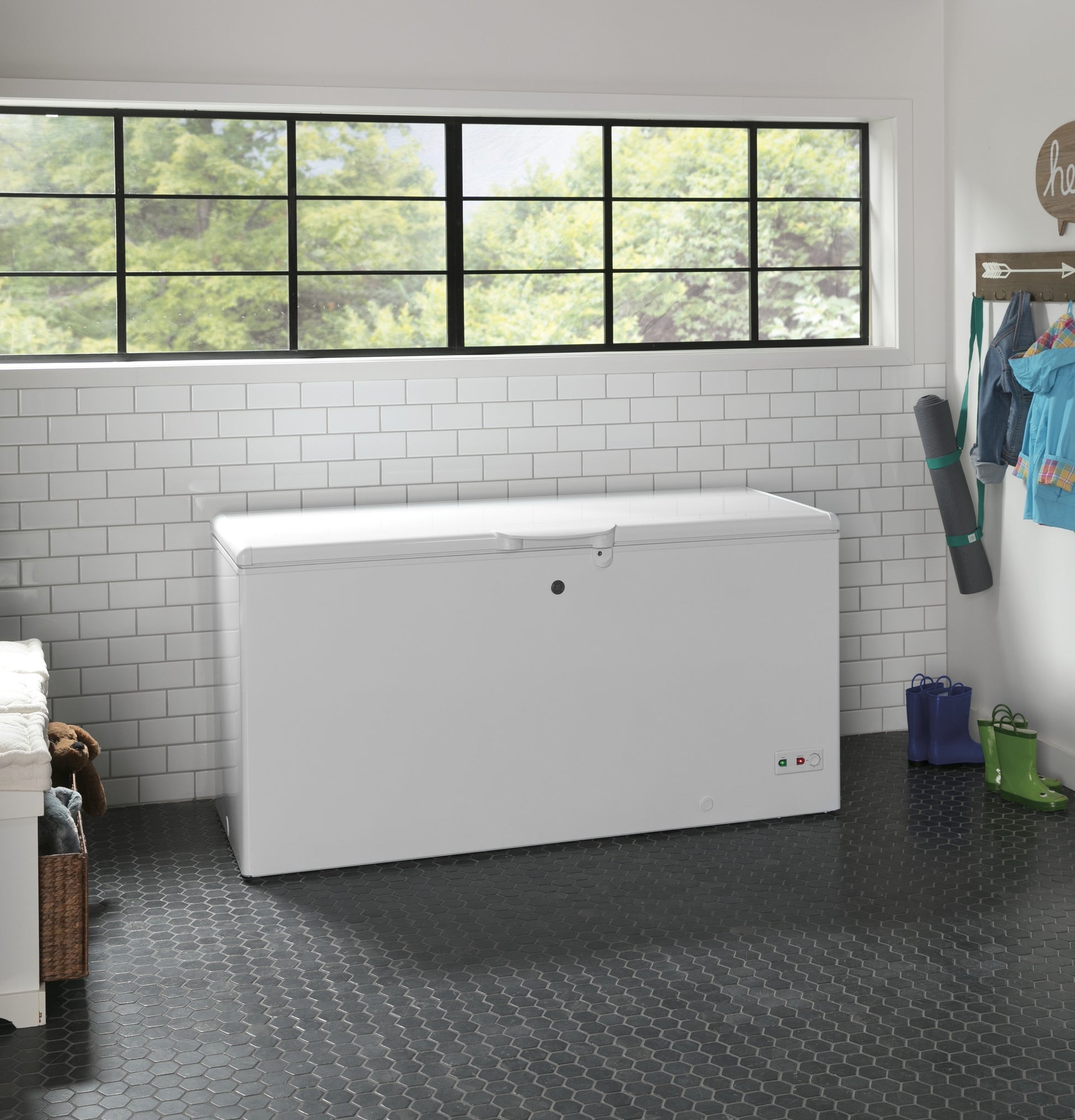 White chest freezer with lock and indicator lights in bright kitchen with tiled wall and large window above