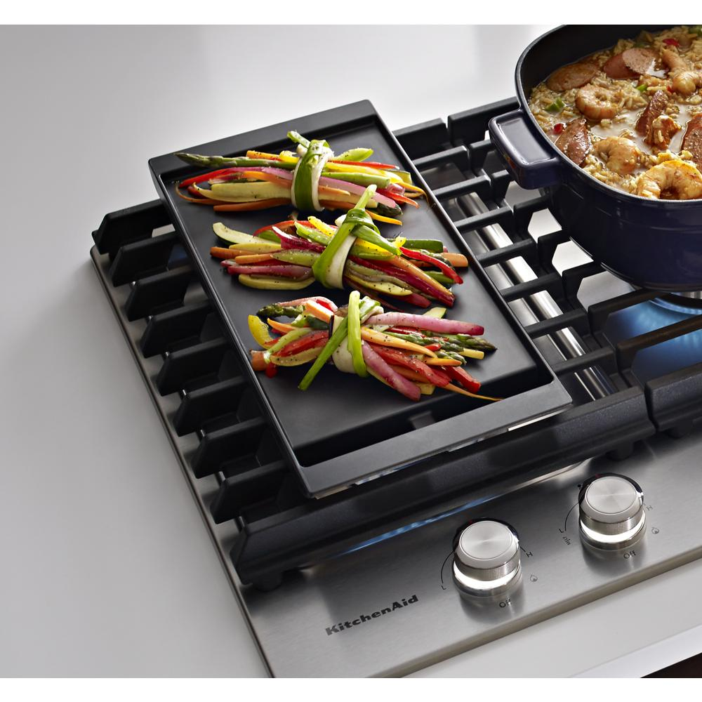 Griddle surface on stainless steel cooktop with vegetable bundles cooking and cast iron grates in kitchenware setting