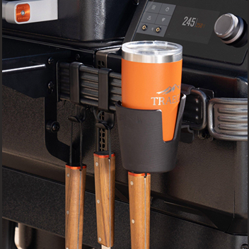 Black plastic cup holder attached to grill with stainless steel tumbler for outdoor grilling and lawn accessories.