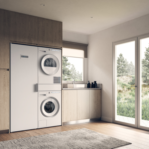 Stacked white washer and dryer set integrated into wooden cabinetry in bright laundry room with natural light.