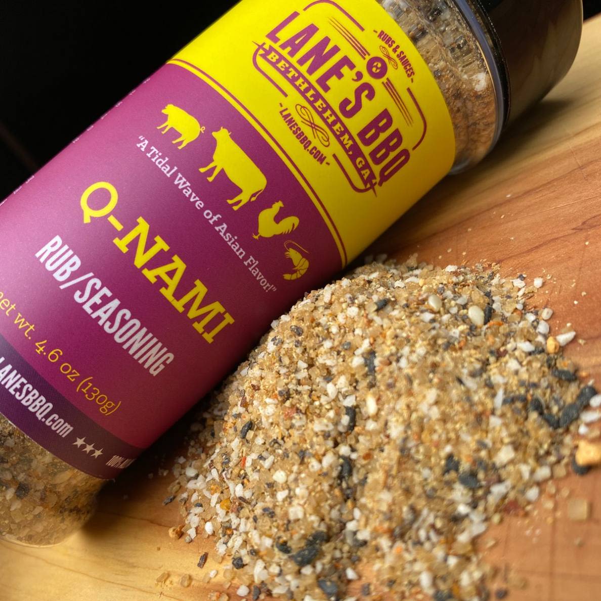 Purple and yellow bottle of Lane's Q-NAMI Rub seasoning spilled on wooden surface for BBQ spices and grilling collections