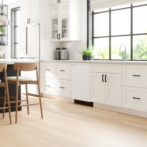Bright kitchen with white cabinetry, wooden chairs, and a built-in white dishwasher under a large window from Bosch appliances collection