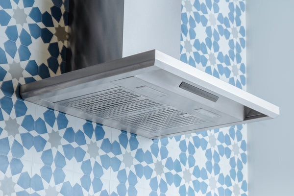 Stainless steel pyramid chimney wall hood mounted on wall with blue geometric tile backsplash in modern kitchen