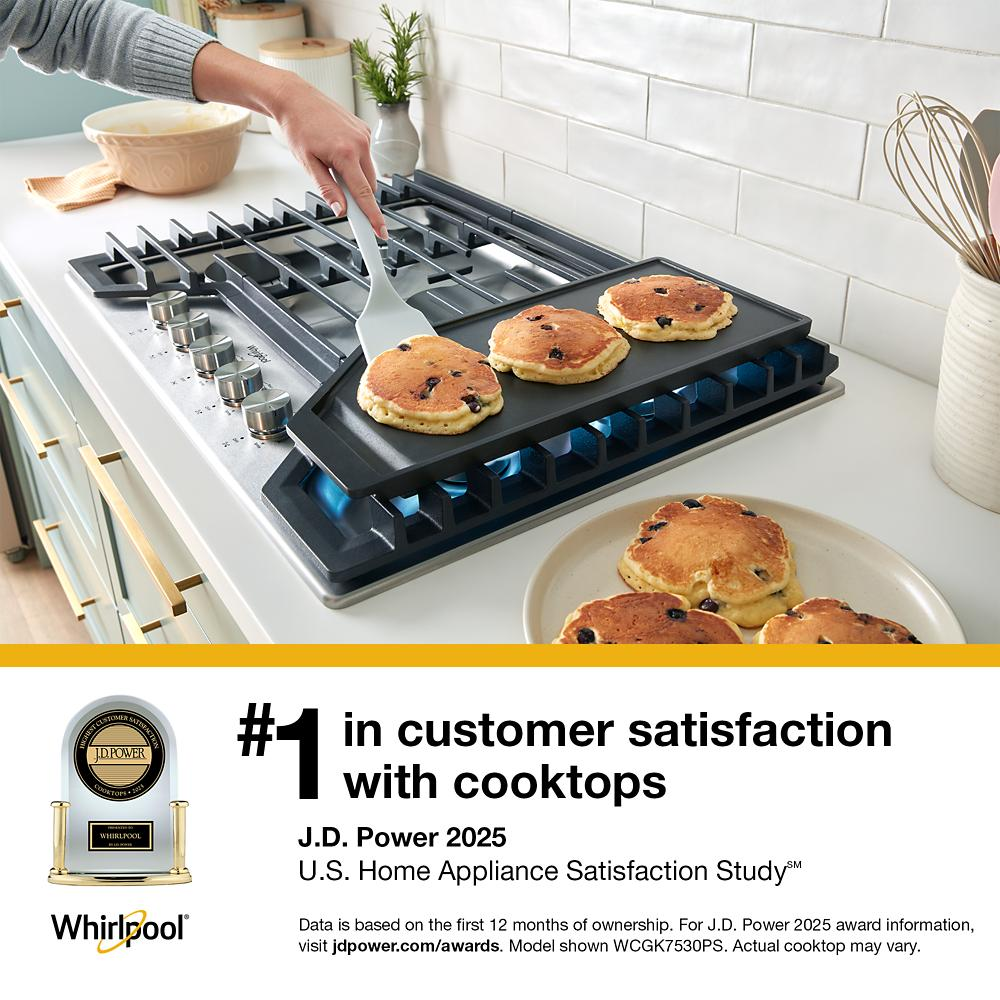 Person flipping blueberry pancakes on a gas cooktop with hinged cast-iron grates in a bright kitchen setting