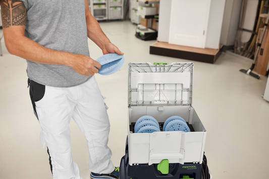 Person holding blue perforated sanding discs next to open gray and green Festool Granat abrasives Systainer in workshop