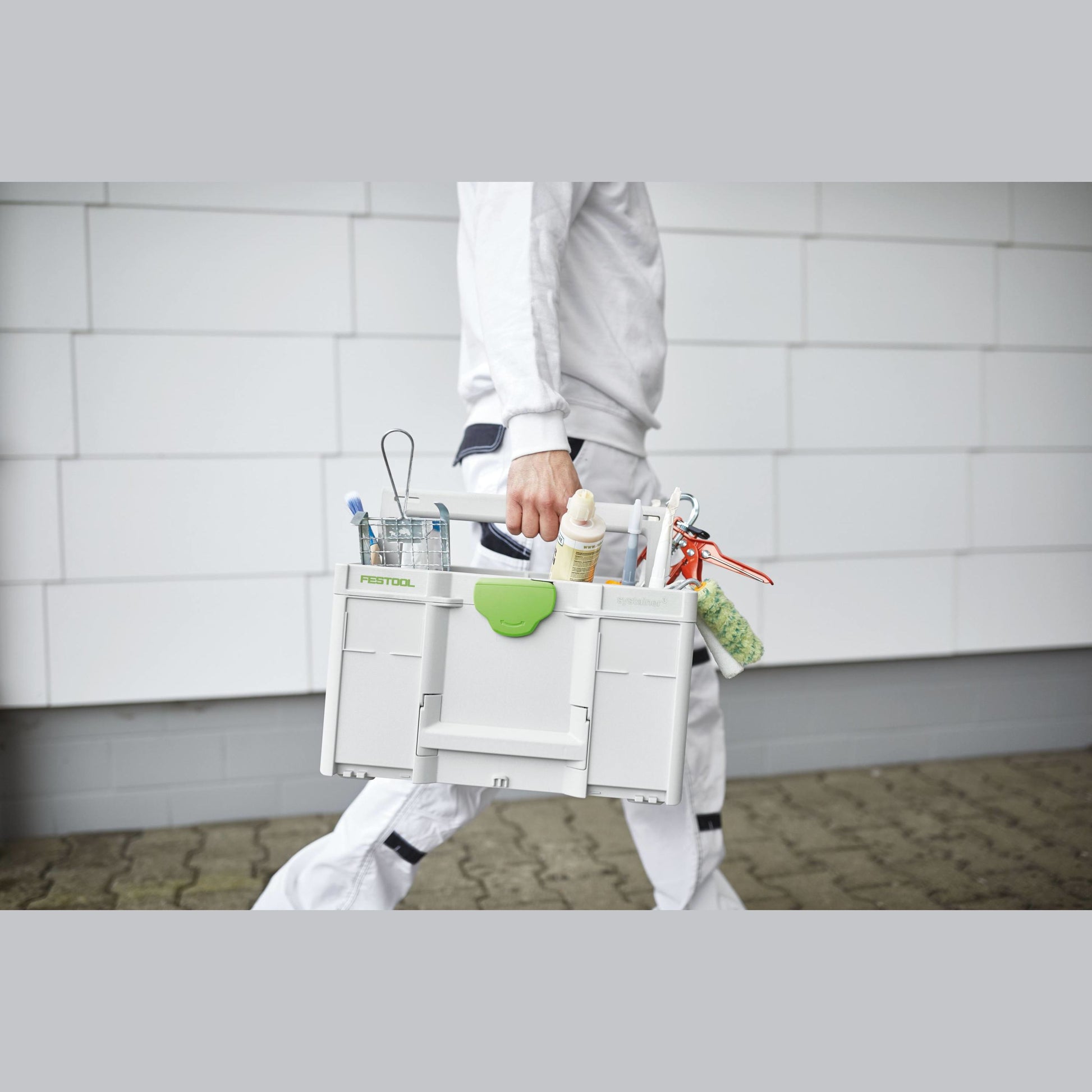 Person carrying a white and green Festool tool storage box filled with painting and home improvement tools outdoors