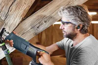 Man wearing blue cordless Bluetooth earplugs using power tool for safety in a wood workshop