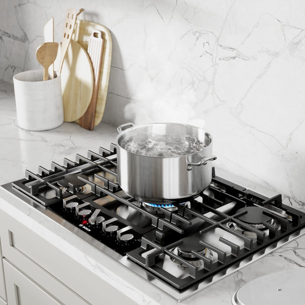 Stainless steel gas cooktop with five burners, boiling pot, and marble countertop in modern kitchen setting