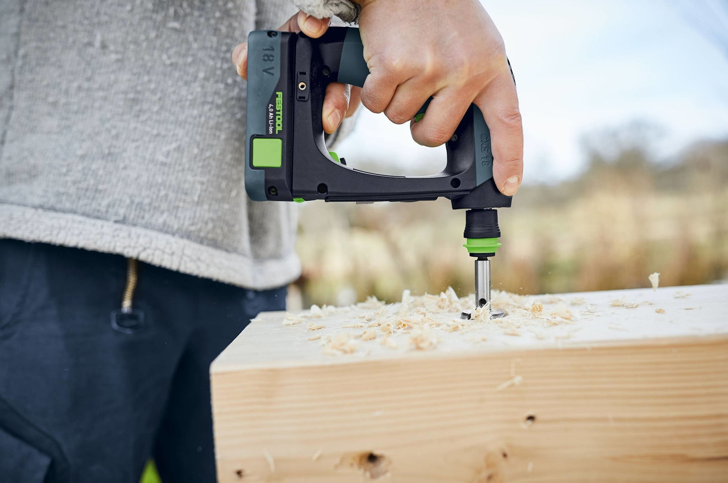 Person using compact cordless drill on wood with sawdust, suitable for woodworking and power tools use