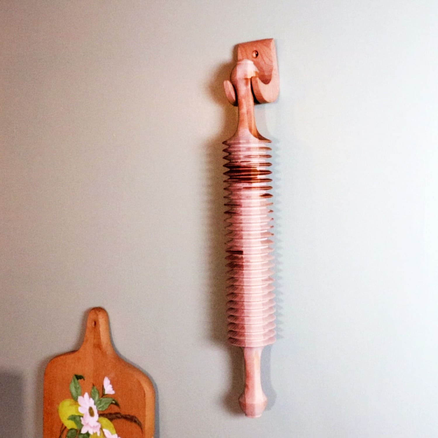 Unfinished cherry wood noodle cutter with carved handle mounted on a kitchen wall in a homeware setting
