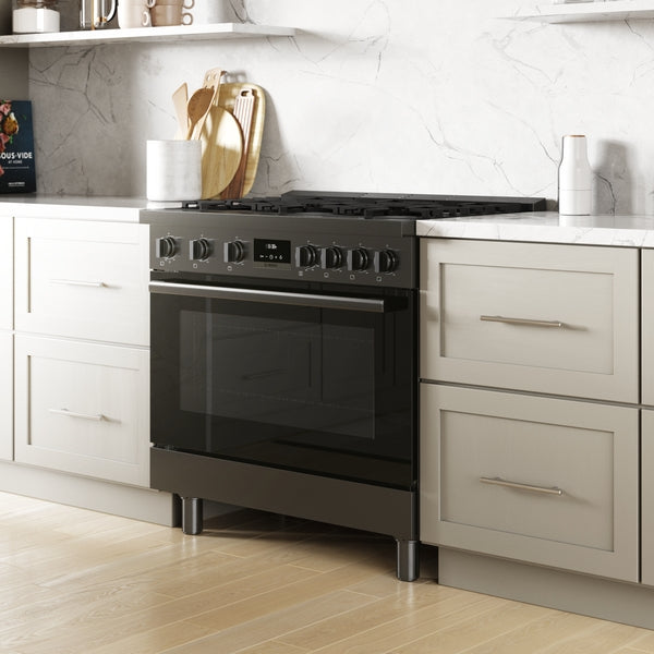 Black stainless steel freestanding gas range with heavy-duty knobs set between light gray kitchen cabinetry and marble countertop