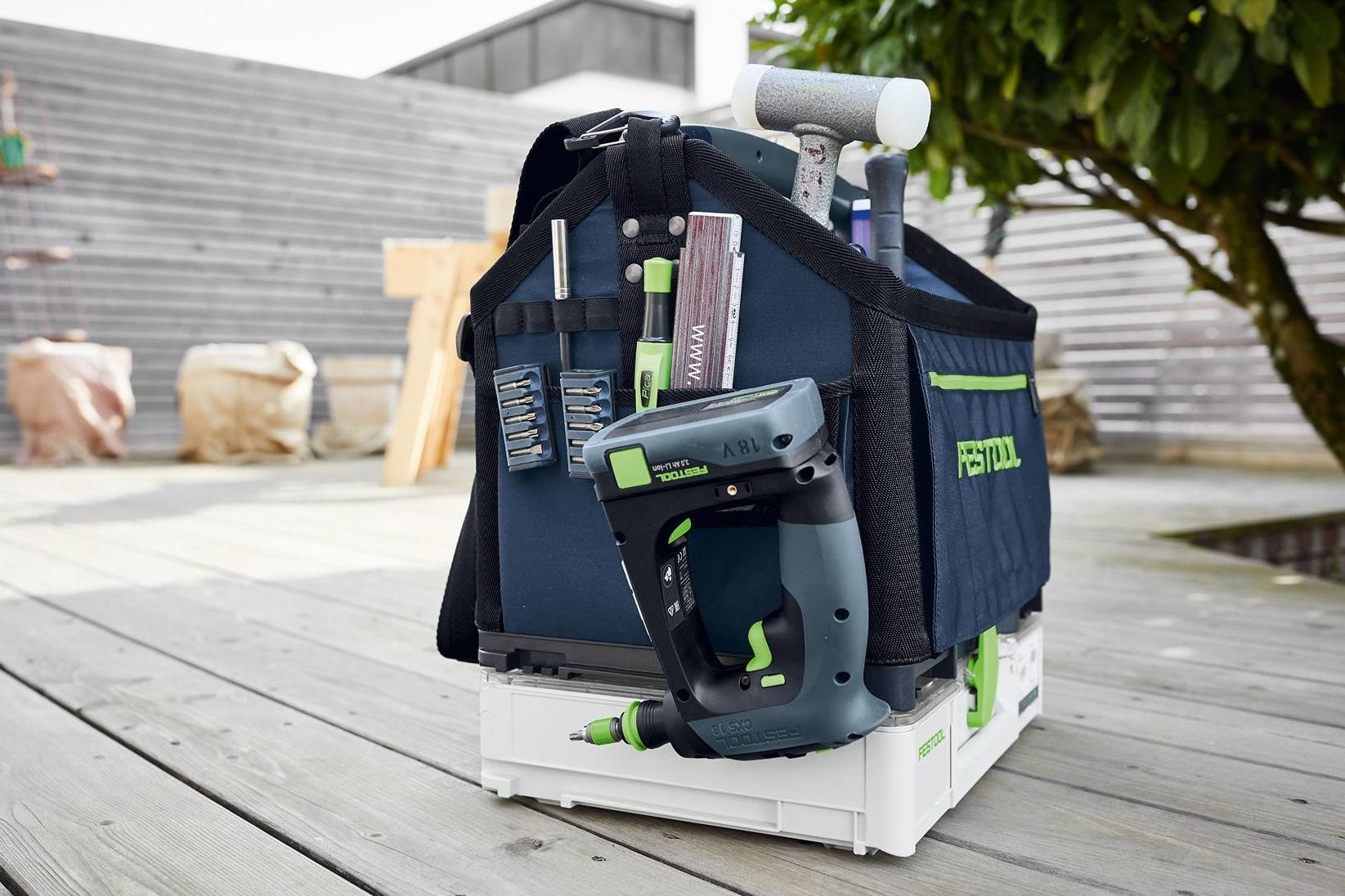 Compact cordless drill with drill bits and hand tools in a navy blue tool bag on a wooden deck for home improvement.