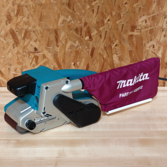 Makita corded belt sander with teal body and maroon dust collection bag for woodworking and home improvement tasks