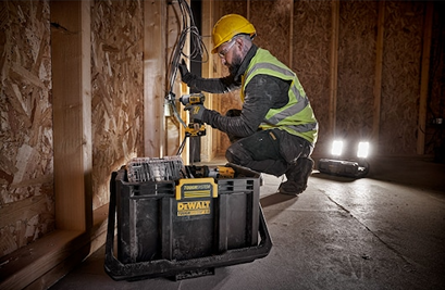 Construction worker using power drill near DEWALT Toughsystem 2.0 adjustable work light illuminating unfinished room