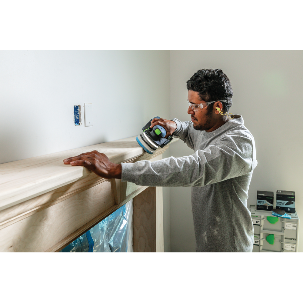 Man wearing safety glasses using Festool power sander on wooden fireplace mantel in tool accessories for home improvement