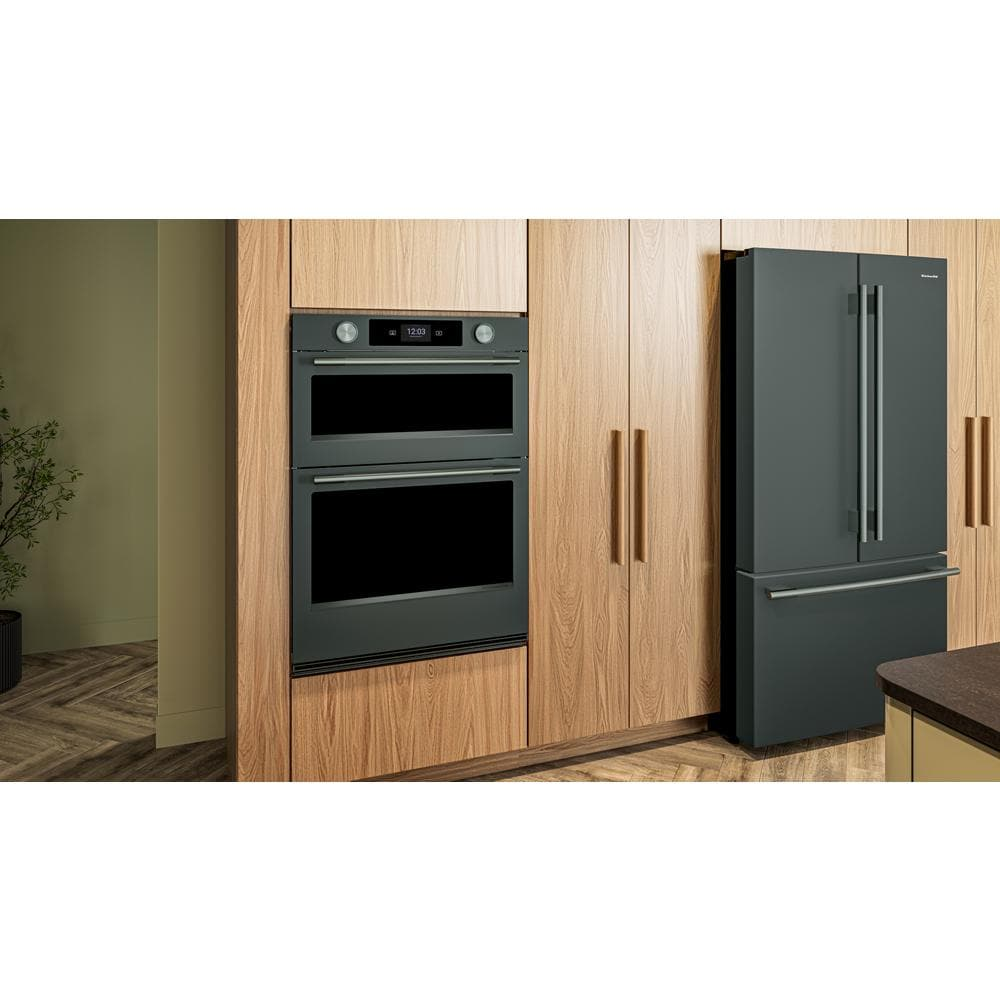 Matte dark green double wall oven integrated into wood cabinetry next to matching refrigerator in modern kitchen.