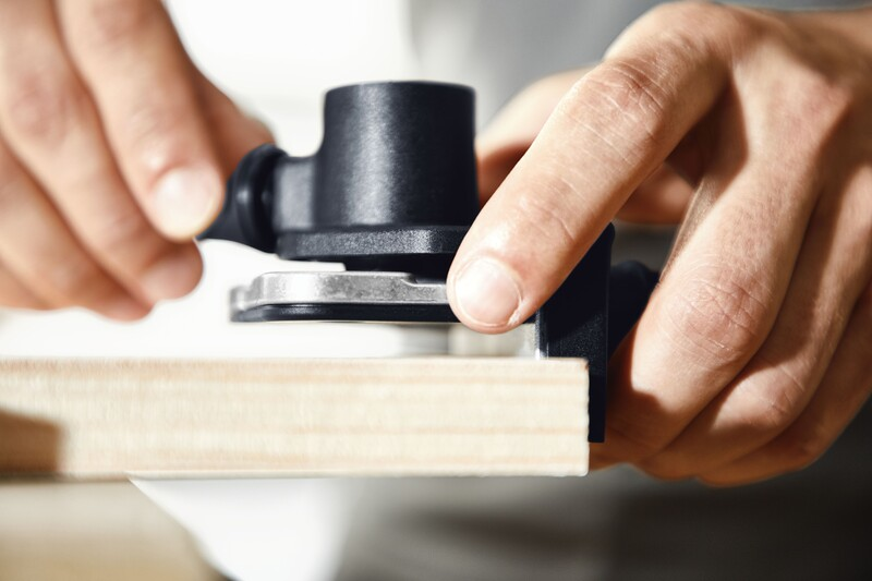 Hands adjusting a black drilling template accessory on wood for precise joinery in woodworking tool collections