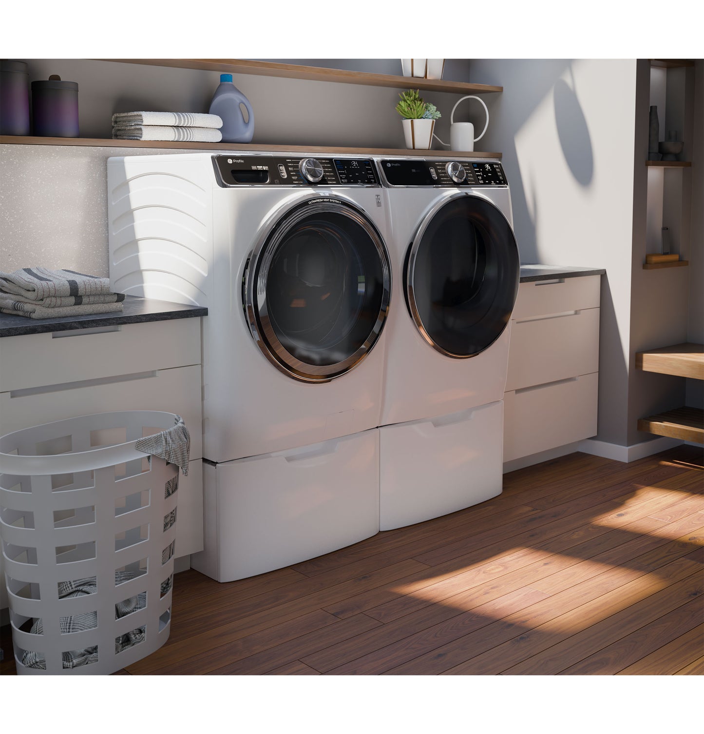 White front load washer and dryer pair with pedestal drawers in bright, modern laundry room featuring wood flooring and open shelving