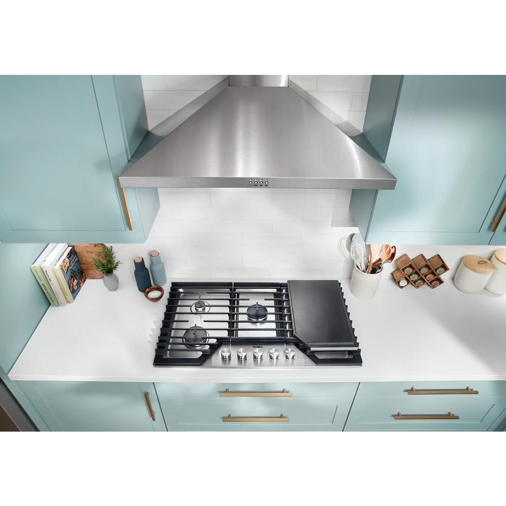 Stainless steel wall mount range hood above black gas cooktop with teal cabinetry in modern kitchen setting