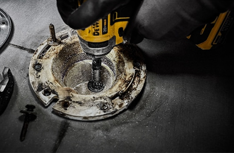 Close-up of a DEWALT tool with hole saw attachment cutting a circular hole in metal for home improvement use
