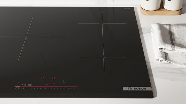 Sleek black Bosch induction cooktop with touch controls on a marble countertop next to folded kitchen towels