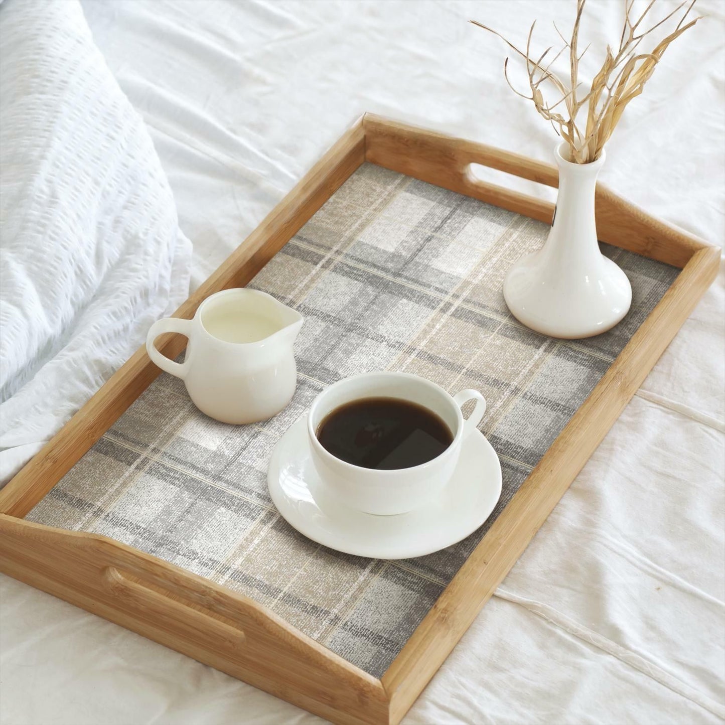 Wooden serving tray with gray tweed plaid patterned liner holding coffee cup, cream pitcher, and white vase with dried grass
