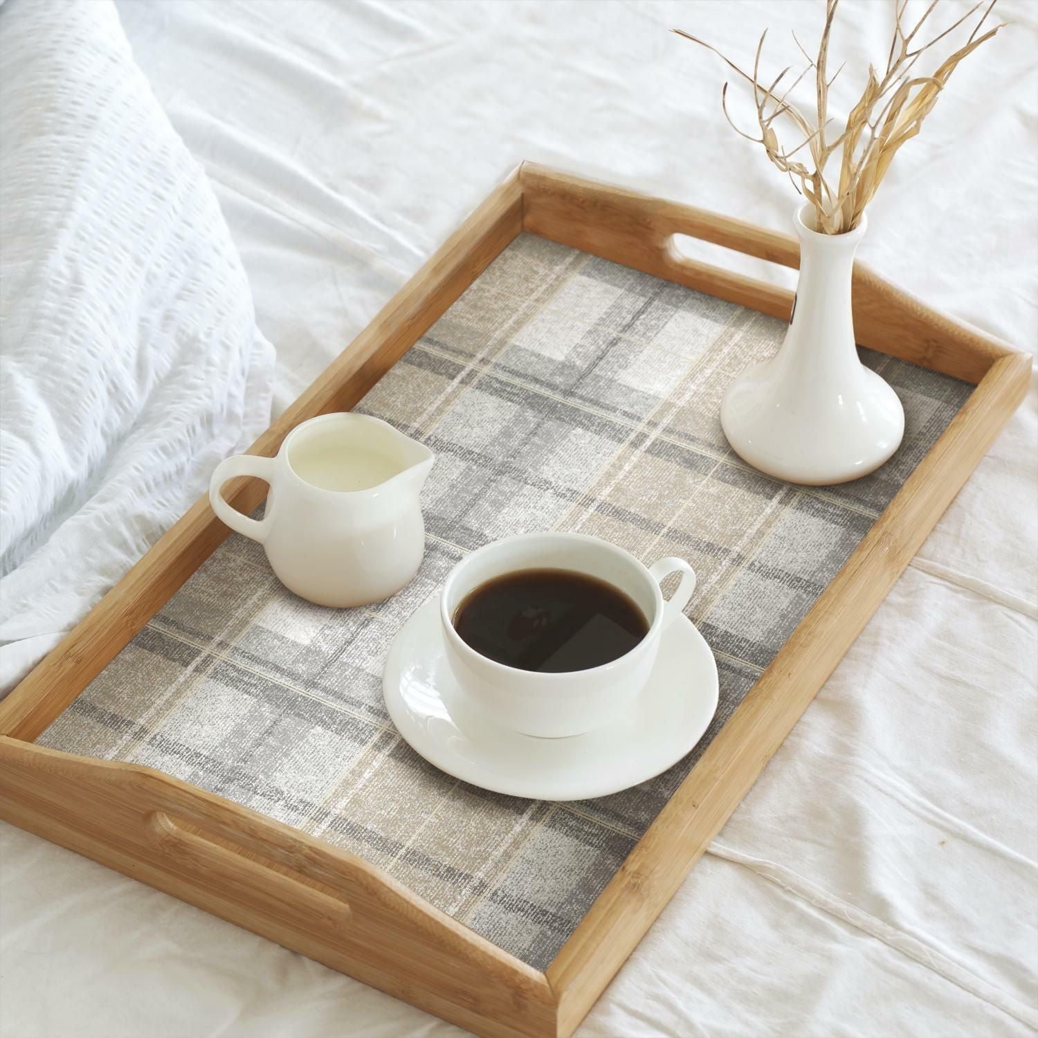 Wooden serving tray with gray tweed plaid patterned liner holding coffee cup, cream pitcher, and white vase with dried grass