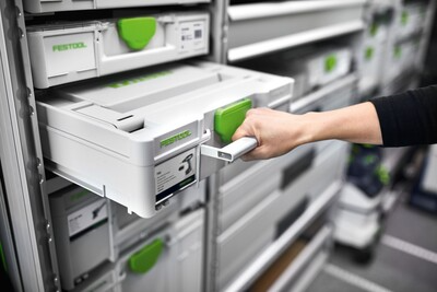 Hand pulling white and green Festool Systainer3 drawer from organized workshop storage shelving system for tool storage and mobility