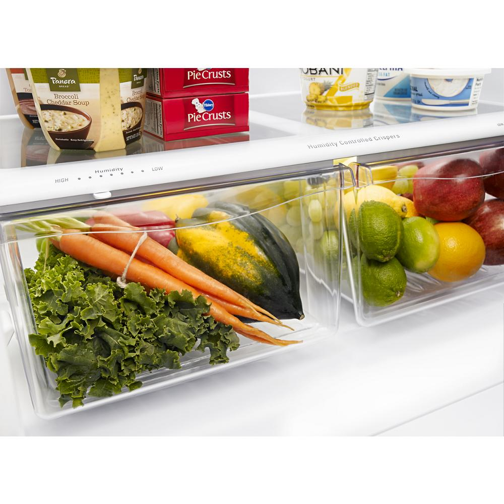 Clear refrigerator humidity-controlled drawers filled with fresh kale, carrots, squash, apples, limes, and lemons in kitchen appliance setting