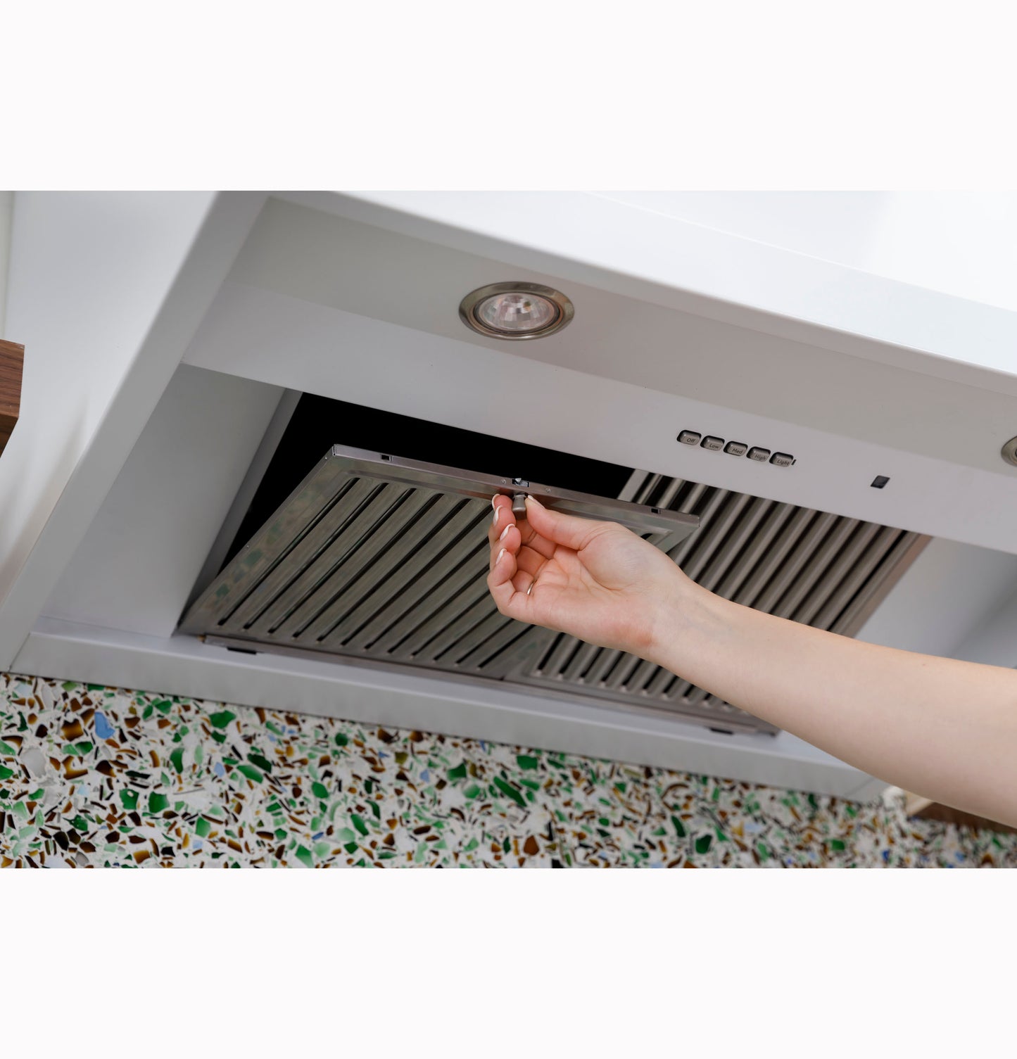 Hand adjusting stainless steel filter of built-in over the range commercial kitchen hood above stove with mosaic backsplash