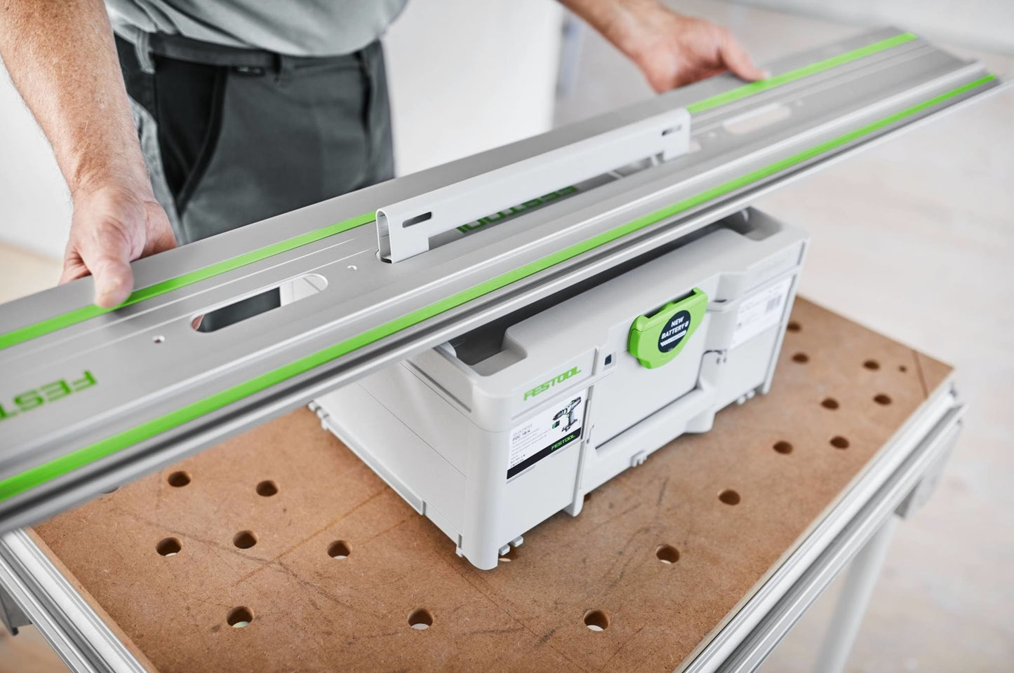 Person positioning a Festool guide rail over a portable storage box on a perforated workbench in a workshop
