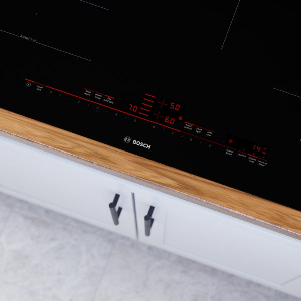 Close-up of Bosch induction cooktop control panel with red digital settings on black glass surface in modern kitchen