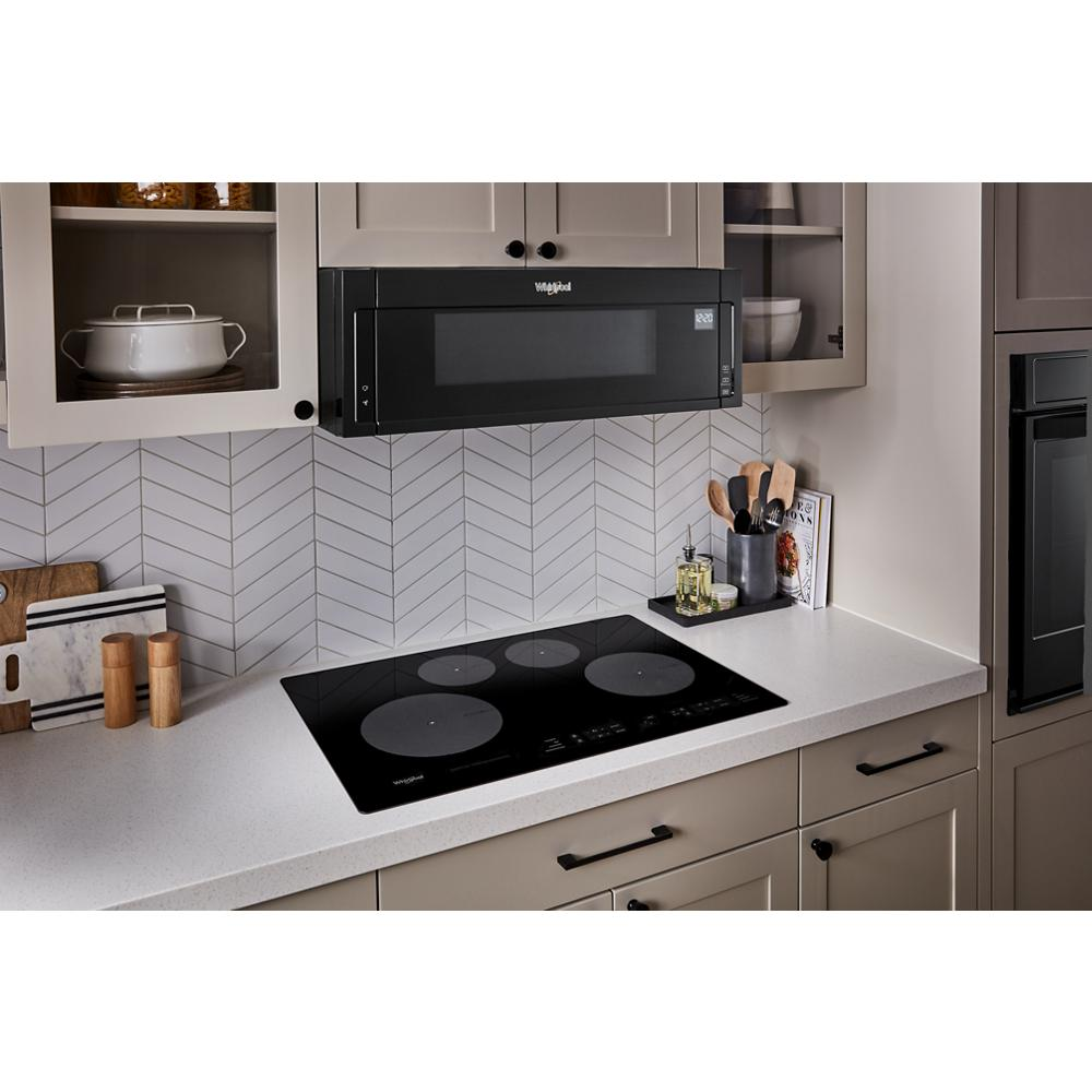 Black glass 30-inch induction cooktop with four heating zones set in light kitchen countertop and cabinetry