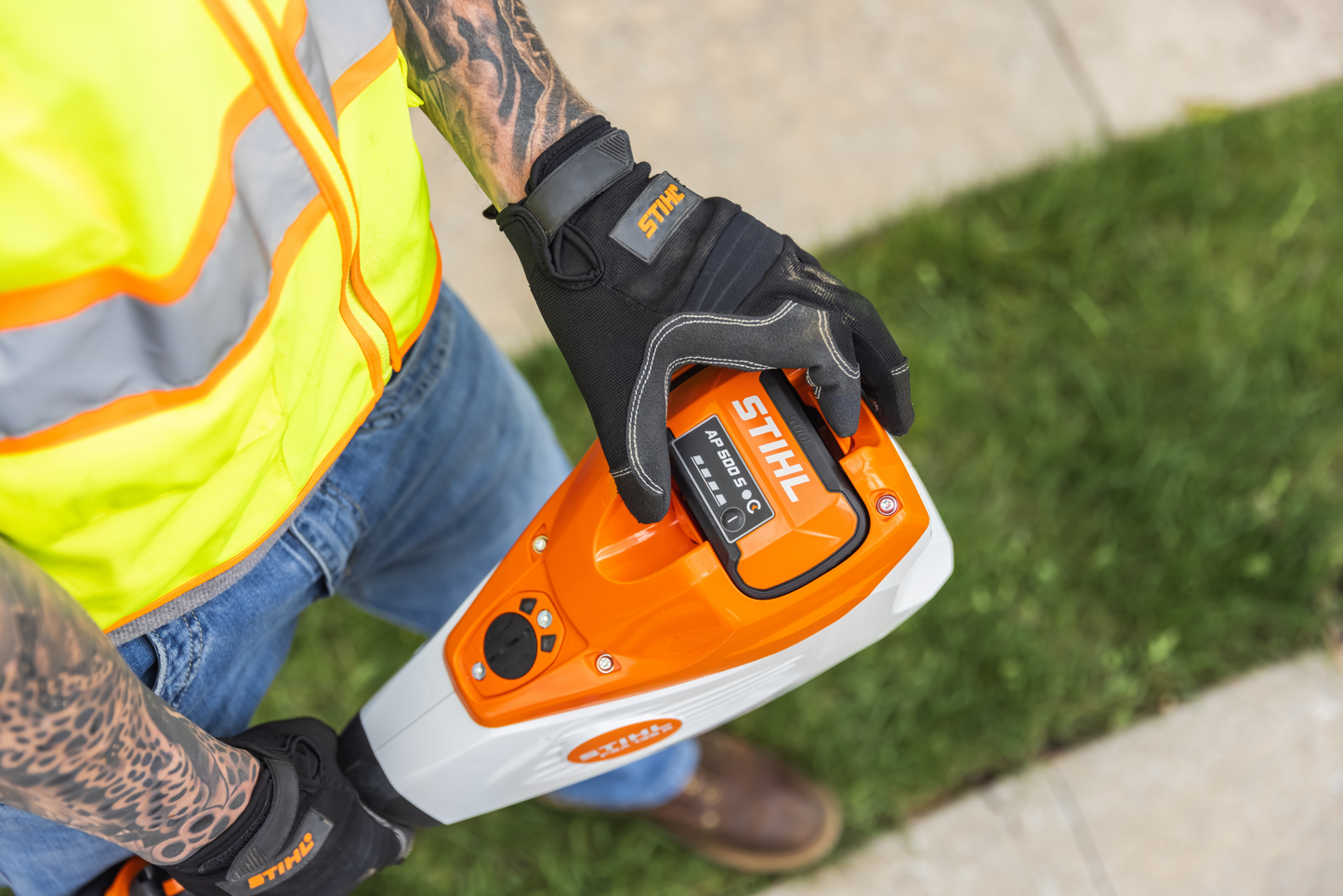Person wearing gloves inserting battery into orange and white STIHL battery-powered trimmer for home improvement tasks