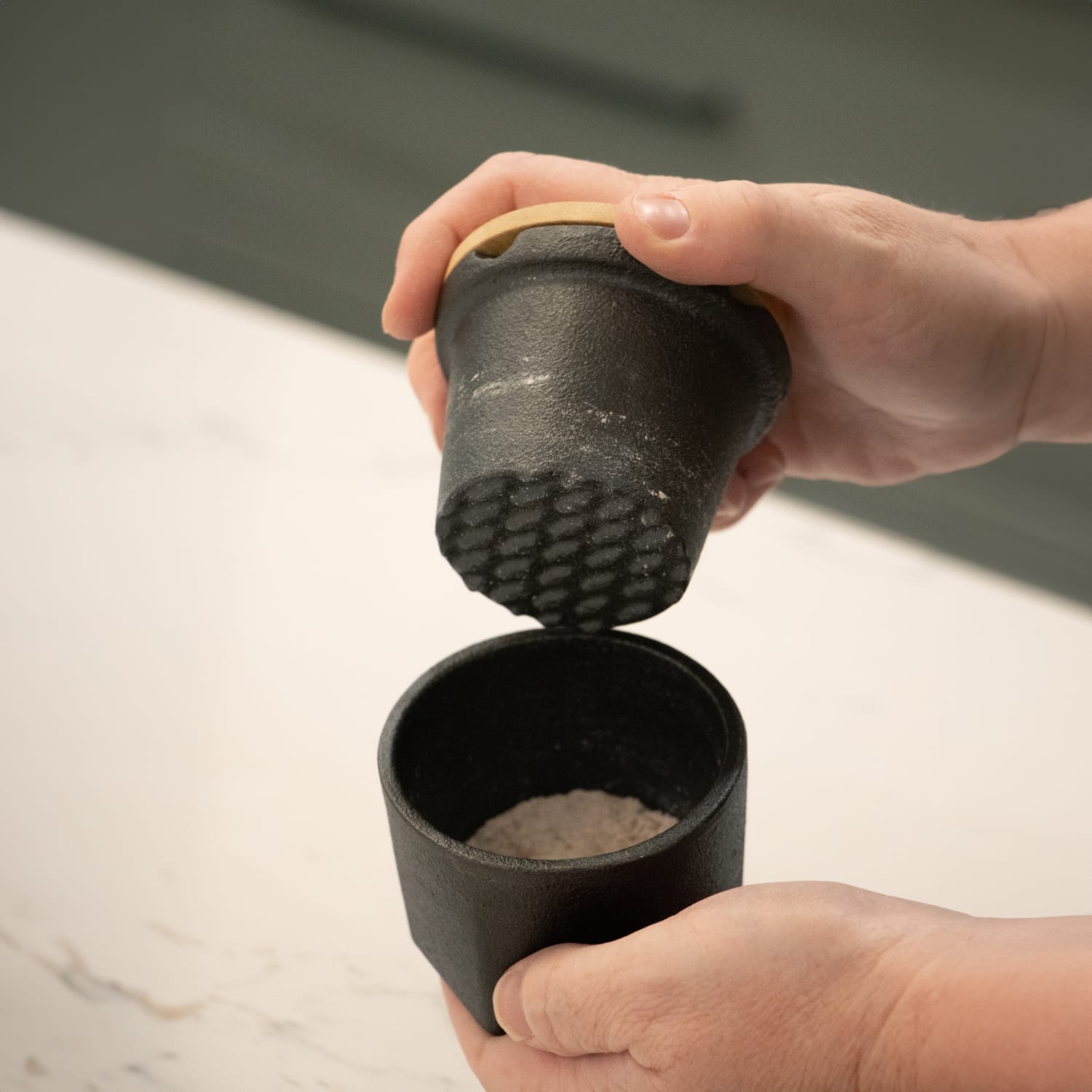 Hands holding a cast iron spice grinder with textured grinding surface and coarse salt inside kitchen gadgets under $50
